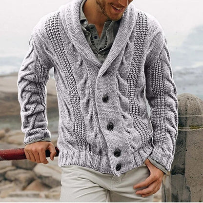 Uomo con cardigan grigio a maglia grossa, bottoni scuri, su sfondo marino. Moda invernale, abbigliamento casual elegante, stile maschile.