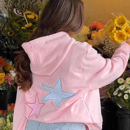 Donna con felpa rosa con stelle, di fronte a fiori colorati. Moda casual, abbigliamento femminile, shopping fiori, stile giovane.