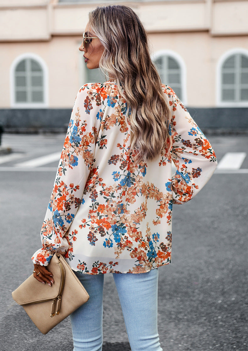 Donna con camicia floreale colorata, jeans chiari e borsa beige, cammina in città. Moda autunnale, stile casual chic, capelli ondulati.