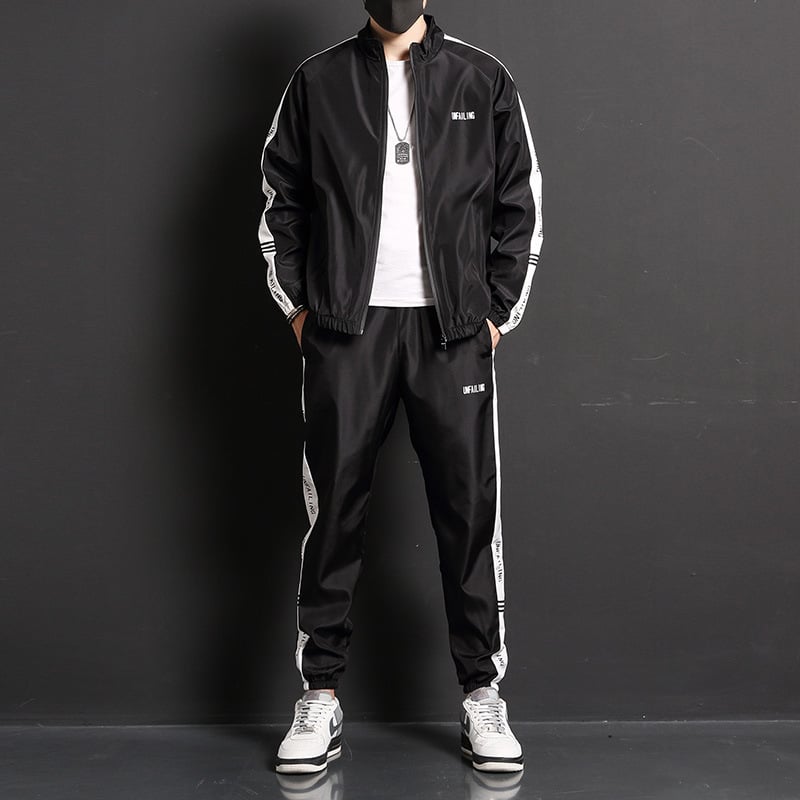 Uomo in tuta sportiva nera con strisce bianche, giacca e pantaloni abbinati, scarpe da ginnastica bianche, sfondo nero. Moda casual maschile.