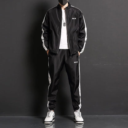 Uomo in tuta sportiva nera con strisce bianche, giacca e pantaloni abbinati, scarpe da ginnastica bianche, sfondo nero. Moda casual maschile.