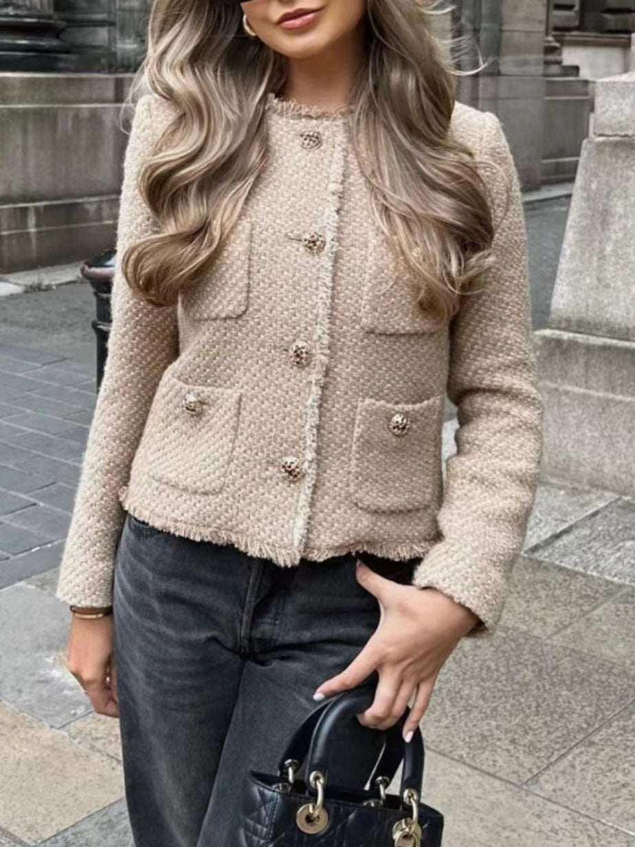 Donna con giacca in tweed beige, bottoni dorati, capelli ondulati, jeans scuri, borsa nera. Moda autunnale elegante in città.