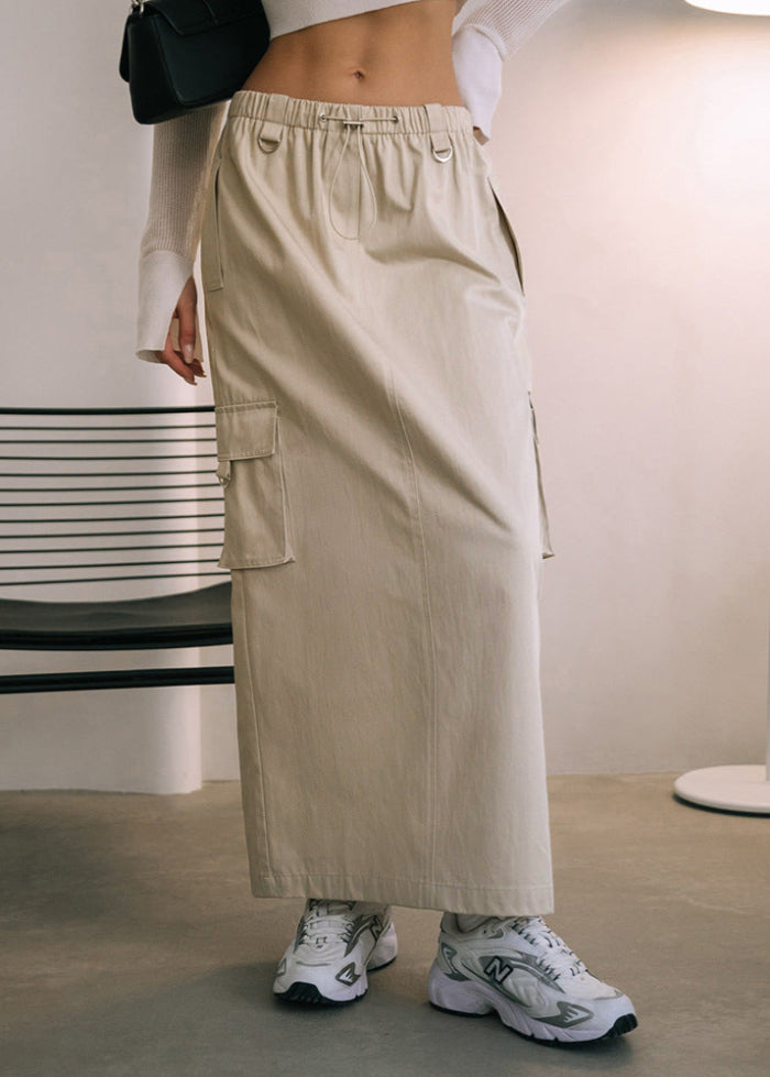Gonna lunga beige con tasche cargo, abbinata a sneakers bianche e maglia bianca a maniche lunghe. Stile casual moderno, moda donna autunno.