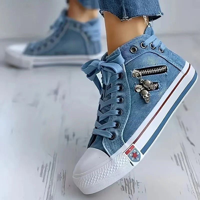 Scarpe da ginnastica alte in denim blu con cerniera e decorazioni a teschio, suola bianca e dettagli rossi, indossate con jeans.