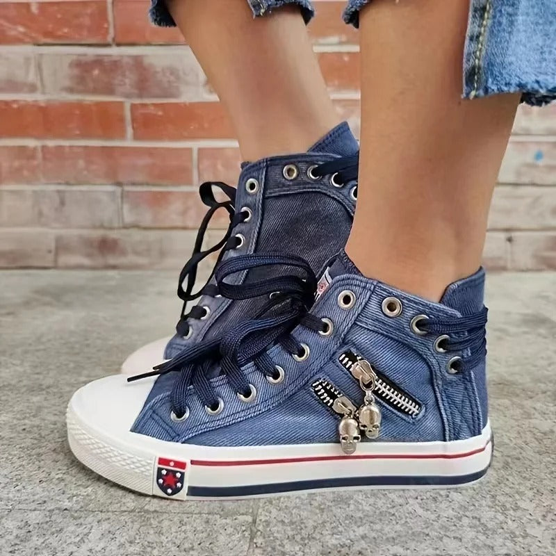 Scarpe da ginnastica alte in denim blu con lacci neri, cerniera decorativa e charm, indossate con jeans strappati. Stile casual urbano.