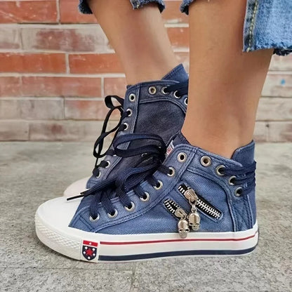 Scarpe da ginnastica alte in denim blu con lacci neri, cerniera decorativa e charm, indossate con jeans strappati. Stile casual urbano.