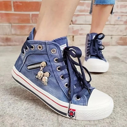 Scarpe da ginnastica alte in denim blu con lacci neri, cerniera laterale e decorazioni a forma di teschio, su sfondo di mattoni.