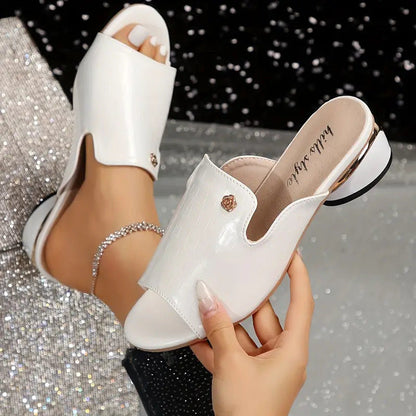 Sandali bianchi eleganti con tacco basso e dettagli dorati, indossati su sfondo scintillante. Scarpe moda donna, stile estivo chic.