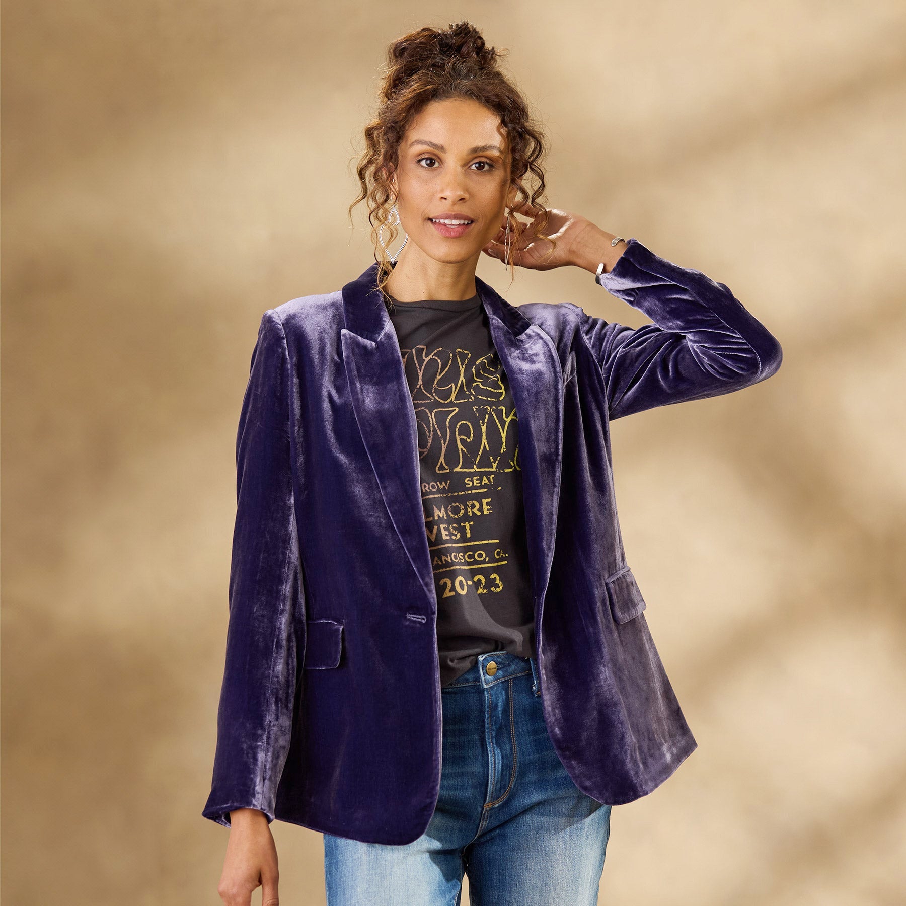 Giacca di velluto viola su donna con capelli ricci, indossa jeans e maglietta grafica. Moda autunnale elegante, stile casual chic.