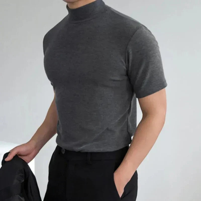 Uomo in maglietta grigia a collo alto, maniche corte, tiene giacca nera. Moda maschile elegante, abbigliamento casual, stile moderno.