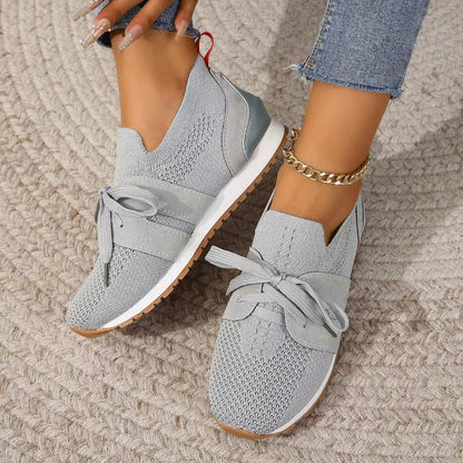 Scarpe da ginnastica grigie da donna, design moderno con lacci, suola bianca e dettagli in maglia, indossate con jeans e cavigliera dorata.