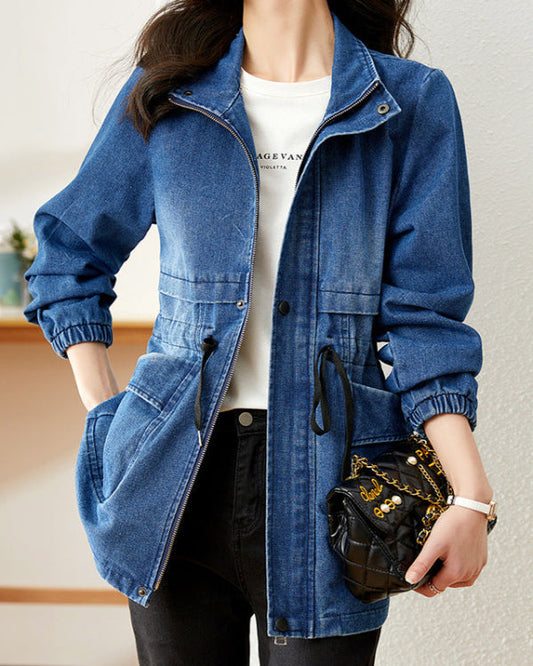 Giacca di jeans blu casual con cerniera, indossata su maglietta bianca. Donna con borsa a tracolla nera trapuntata con catena dorata.