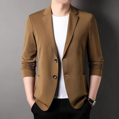 Giacca elegante marrone da uomo su sfondo grigio, abbinata a t-shirt bianca e pantaloni neri. Moda maschile, abbigliamento casual chic.