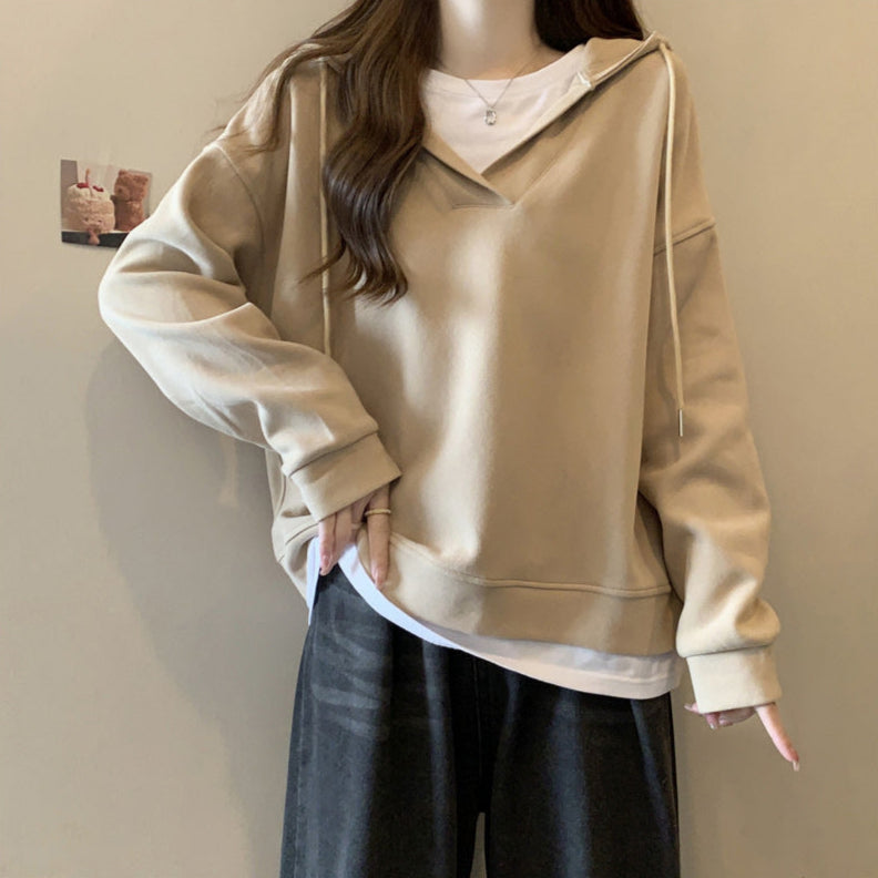 Donna con felpa beige oversize e jeans neri, posa casual. Moda autunnale, abbigliamento comodo, stile urbano. Sfondo neutro.