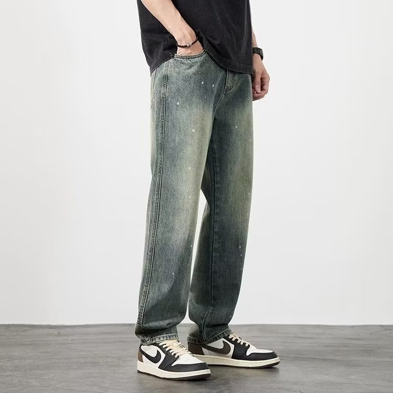 Jeans larghi in denim verde slavato, indossati con scarpe sportive bianche e nere, su sfondo grigio. Moda casual uomo, stile urbano.