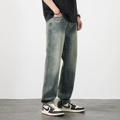 Jeans larghi in denim verde slavato, indossati con scarpe sportive bianche e nere, su sfondo grigio. Moda casual uomo, stile urbano.