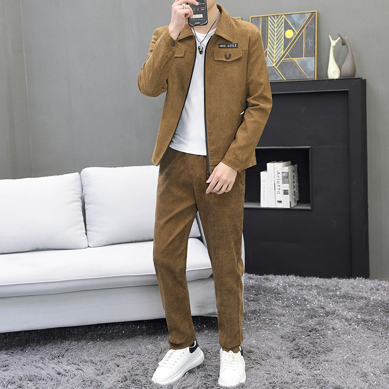 Uomo in tuta marrone scamosciata, camicia bianca e scarpe da ginnastica bianche, in salotto moderno con divano bianco e tappeto grigio.