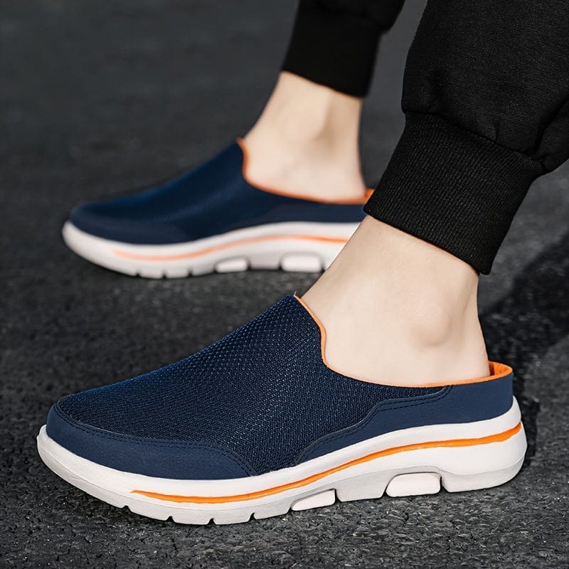 Scarpe slip-on blu da uomo su strada asfaltata, design sportivo con suola bianca e dettagli arancioni, ideali per camminate e tempo libero.