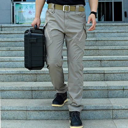 Uomo con pantaloni tattici grigi, scarponi neri, e valigetta nera su scale esterne. Abbigliamento outdoor resistente e funzionale.