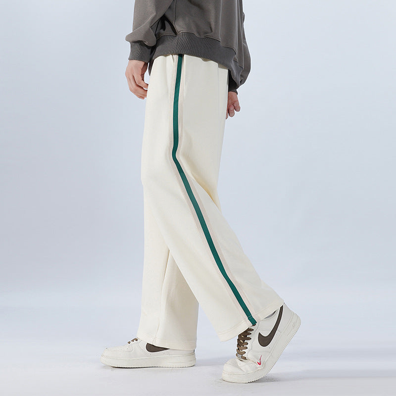Pantaloni bianchi con striscia verde, indossati con scarpe da ginnastica bianche e felpa grigia. Moda casual uomo, stile sportivo elegante.