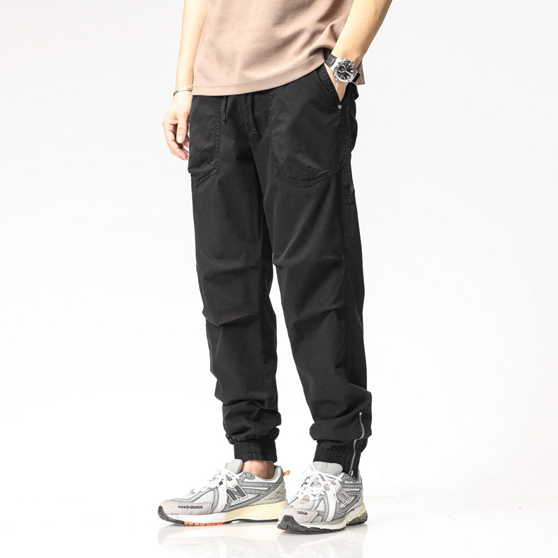Pantaloni cargo neri da uomo, stile casual, con tasche laterali, indossati con scarpe da ginnastica grigie e maglietta beige.