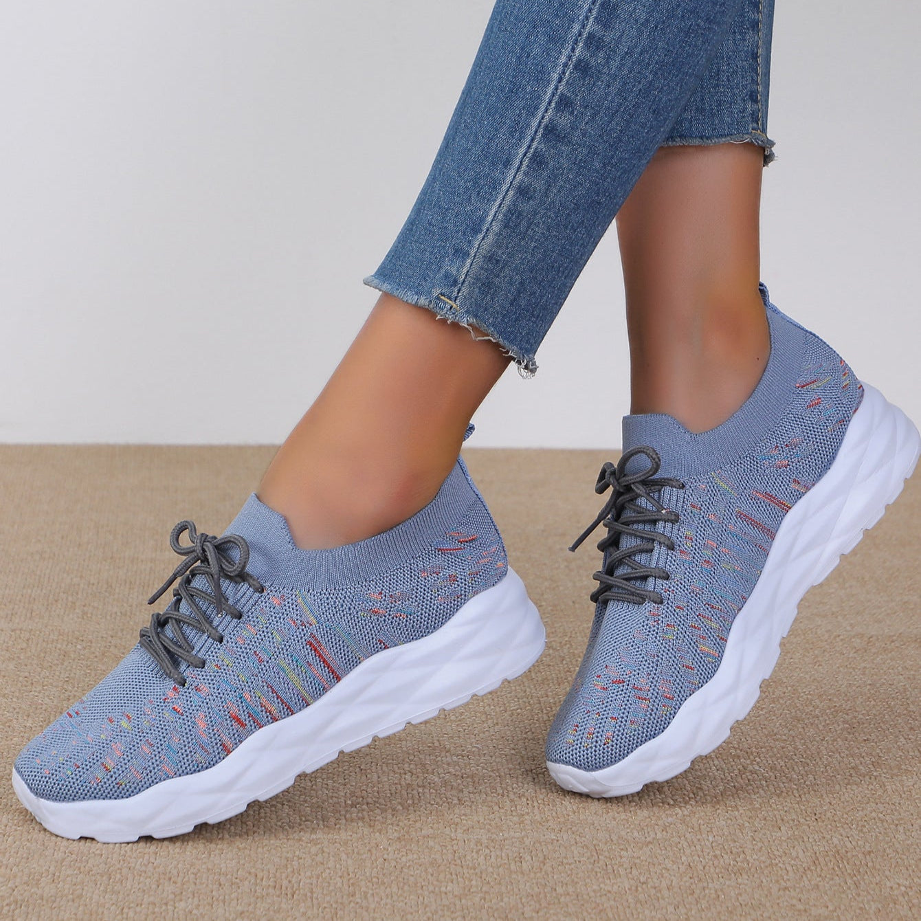 Scarpe da ginnastica grigie da donna con suola bianca, indossate con jeans. Design moderno e confortevole, ideali per attività sportive e casual.