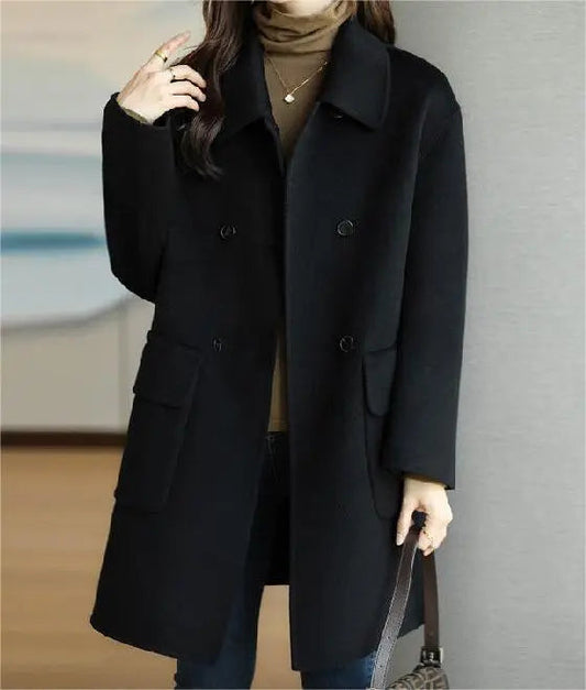 Donna con cappotto nero elegante, doppio petto, tasche grandi, indossa maglione marrone, anello e collana, sfondo sfocato. Moda autunno inverno.