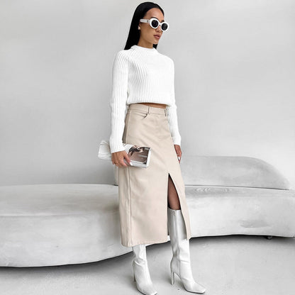 Donna con occhiali da sole bianchi indossa maglione bianco, gonna beige con spacco e stivali alti bianchi. Moda elegante e minimalista.