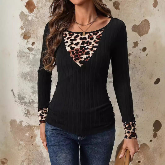 Donna con maglia nera a maniche lunghe, dettagli leopardati su scollo e polsini, indossa jeans. Sfondo con parete effetto vintage.