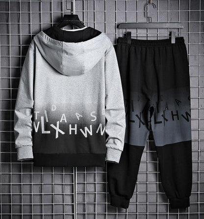 Tuta sportiva uomo grigia e nera con cappuccio, design moderno con lettere, appesa su griglia metallica. Abbigliamento casual alla moda.