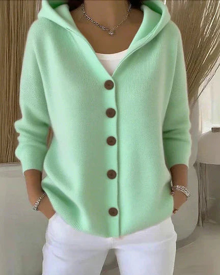 Donna con cardigan verde menta con cappuccio e bottoni marroni, indossa pantaloni bianchi. Moda casual elegante, abbigliamento autunnale.