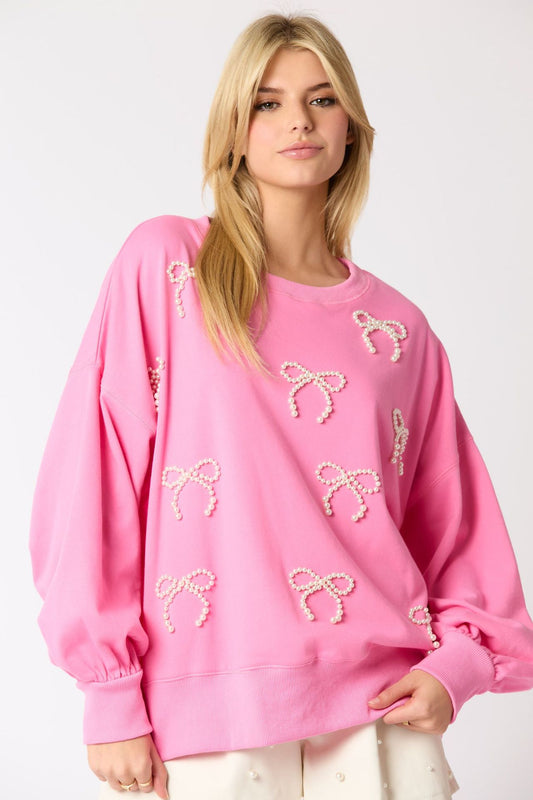 Maglione rosa con fiocchi decorativi, indossato da una donna bionda. Moda casual, abbigliamento femminile trendy, stile autunnale.