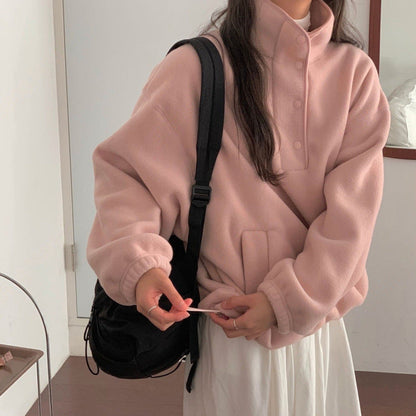 Donna con felpa rosa oversize e zaino nero, in piedi in una stanza minimalista. Moda casual autunnale, abbigliamento comodo e trendy.
