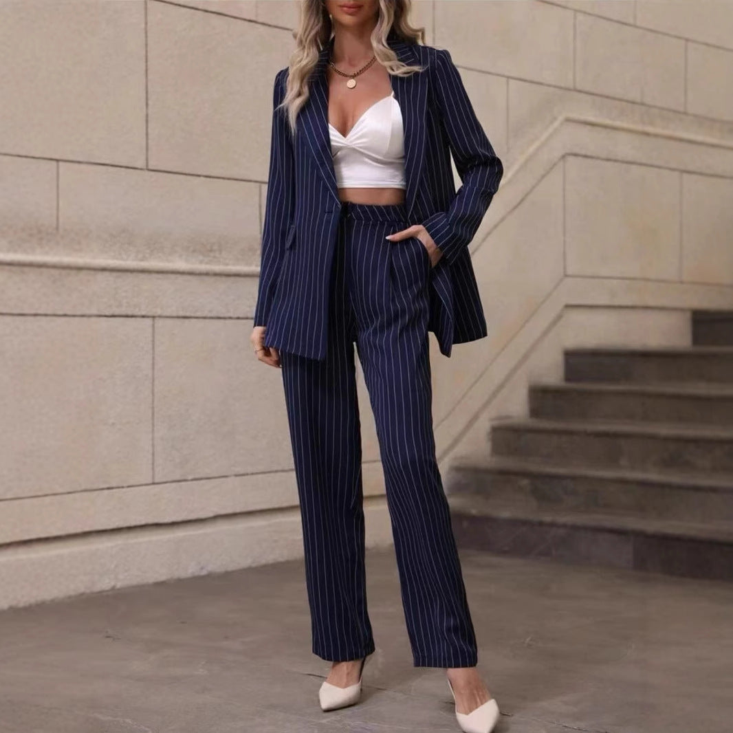 Donna in completo gessato blu scuro, top bianco, tacchi beige, posa su scala interna. Moda elegante, abbigliamento formale femminile, tendenze 2023.