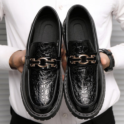 Scarpe mocassini uomo in pelle nera lucida con motivo coccodrillo, dettagli metallici dorati, indossate da persona in camicia bianca.