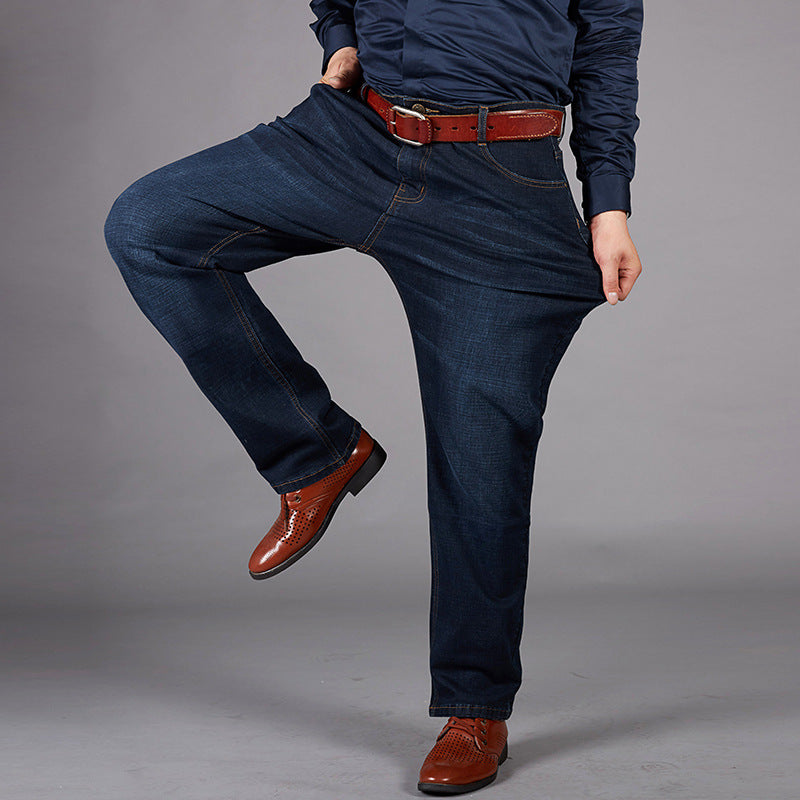 Uomo in jeans larghi blu scuro, camicia blu e scarpe marroni eleganti, posa su sfondo grigio. Moda maschile casual, abbigliamento comodo.
