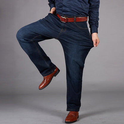 Uomo in jeans larghi blu scuro, camicia blu e scarpe marroni eleganti, posa su sfondo grigio. Moda maschile casual, abbigliamento comodo.