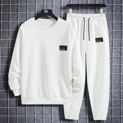 Completo tuta bianco trapuntato, composto da felpa e pantaloni con elastico in vita, appesi su gruccia nera, sfondo a quadri grigi.