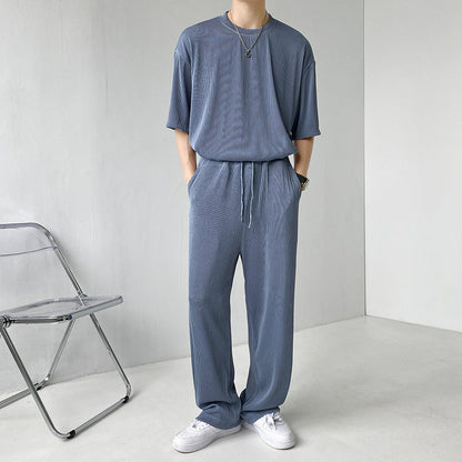 Uomo in tuta grigia casual, con maglietta e pantaloni coordinati, indossa scarpe bianche. Stile minimalista, moda uomo contemporanea.