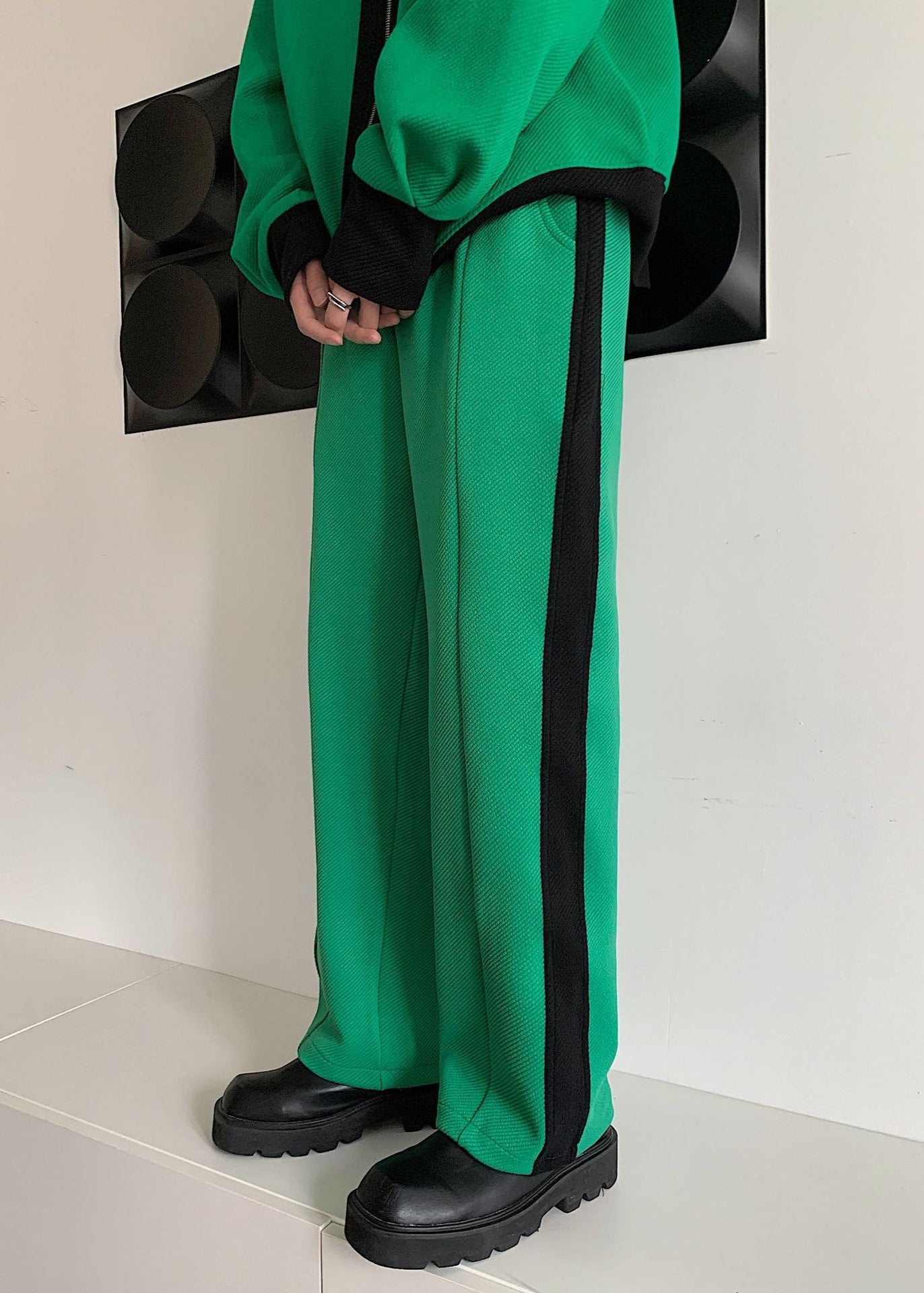 Pantaloni verdi con striscia nera laterale, abbinati a giacca verde. Moda streetwear, stile casual, scarpe nere chunky.
