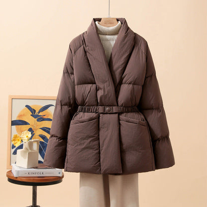 Giacca invernale imbottita marrone su appendiabiti, sfondo beige. Design elegante, cintura in vita, ideale per moda autunnale e invernale.