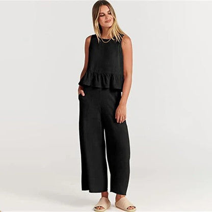 Donna in abbigliamento estivo nero, top senza maniche con volant e pantaloni larghi, sandali beige. Moda casual elegante.