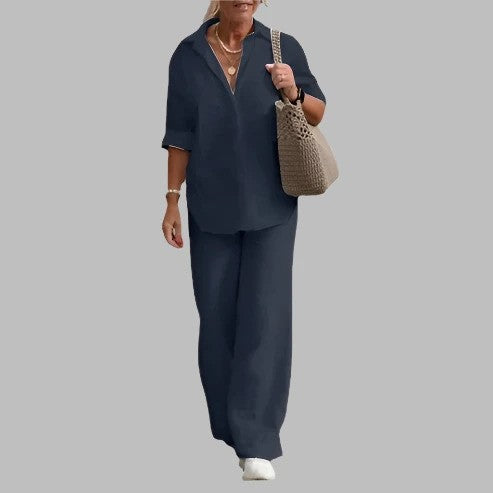 Donna in abbigliamento casual elegante, indossa camicia e pantaloni blu scuro, borsa intrecciata beige, collana e scarpe bianche. Moda donna chic.