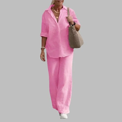Donna in abito estivo rosa, camicia e pantaloni larghi, borsa a tracolla beige, sfondo grigio. Moda casual donna, abbigliamento estivo elegante.