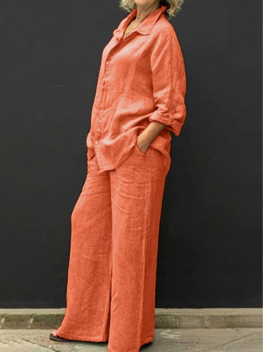 Donna in abito di lino arancione, camicia e pantaloni larghi, sfondo nero. Moda estiva, abbigliamento casual elegante, stile rilassato.