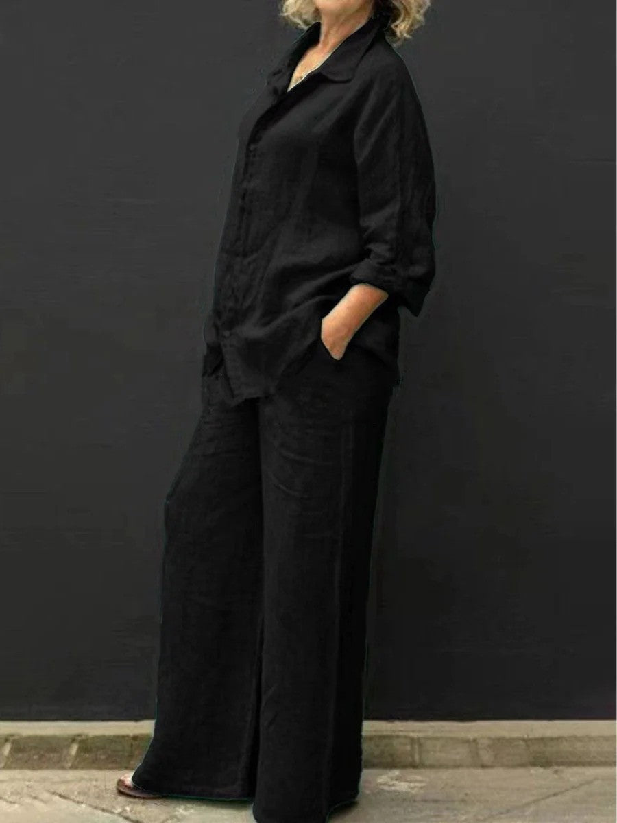 Donna in abbigliamento nero casual, camicia e pantaloni larghi, posa contro sfondo scuro. Moda minimalista, stile elegante e confortevole.