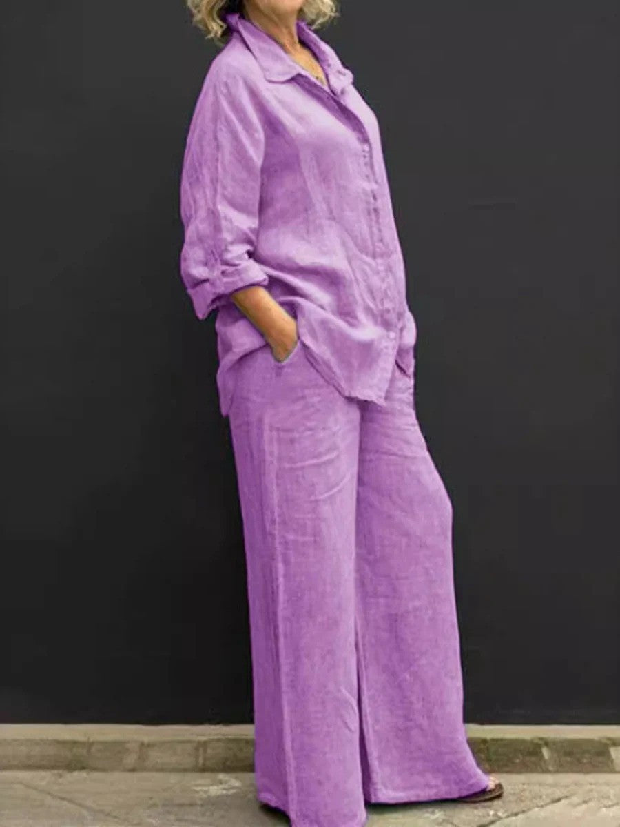 Donna in abito di lino viola, camicia e pantaloni larghi, posa contro sfondo nero. Moda estiva, abbigliamento casual elegante.
