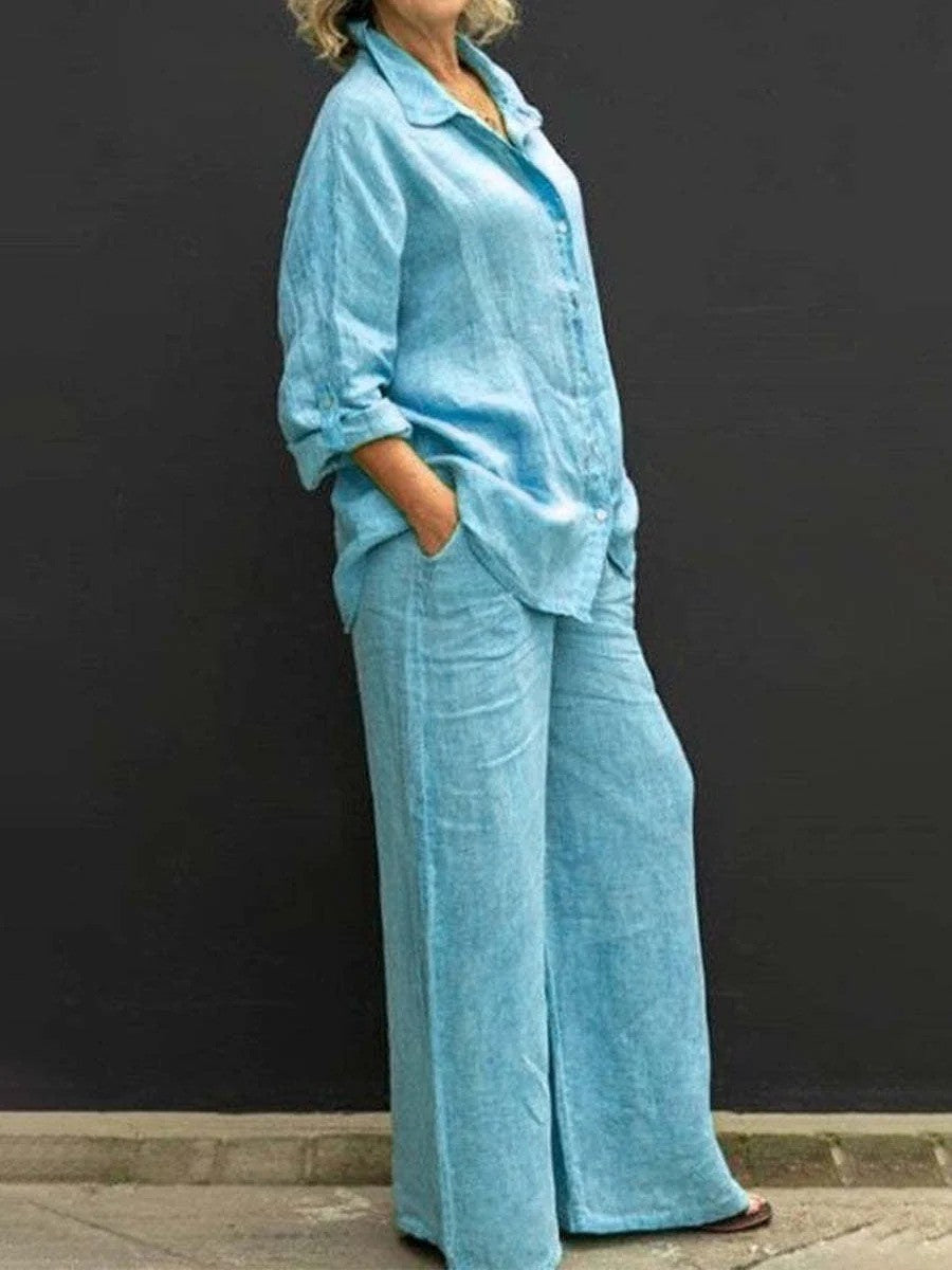 Donna in abbigliamento casual, indossa un completo di lino azzurro con camicia e pantaloni larghi, sfondo nero. Moda estiva, stile rilassato.