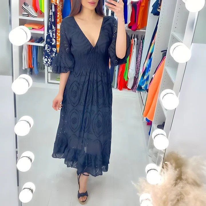Donna in abito nero elegante con scollo a V in camerino illuminato, circondata da abiti colorati. Moda femminile, shopping, abbigliamento estivo.