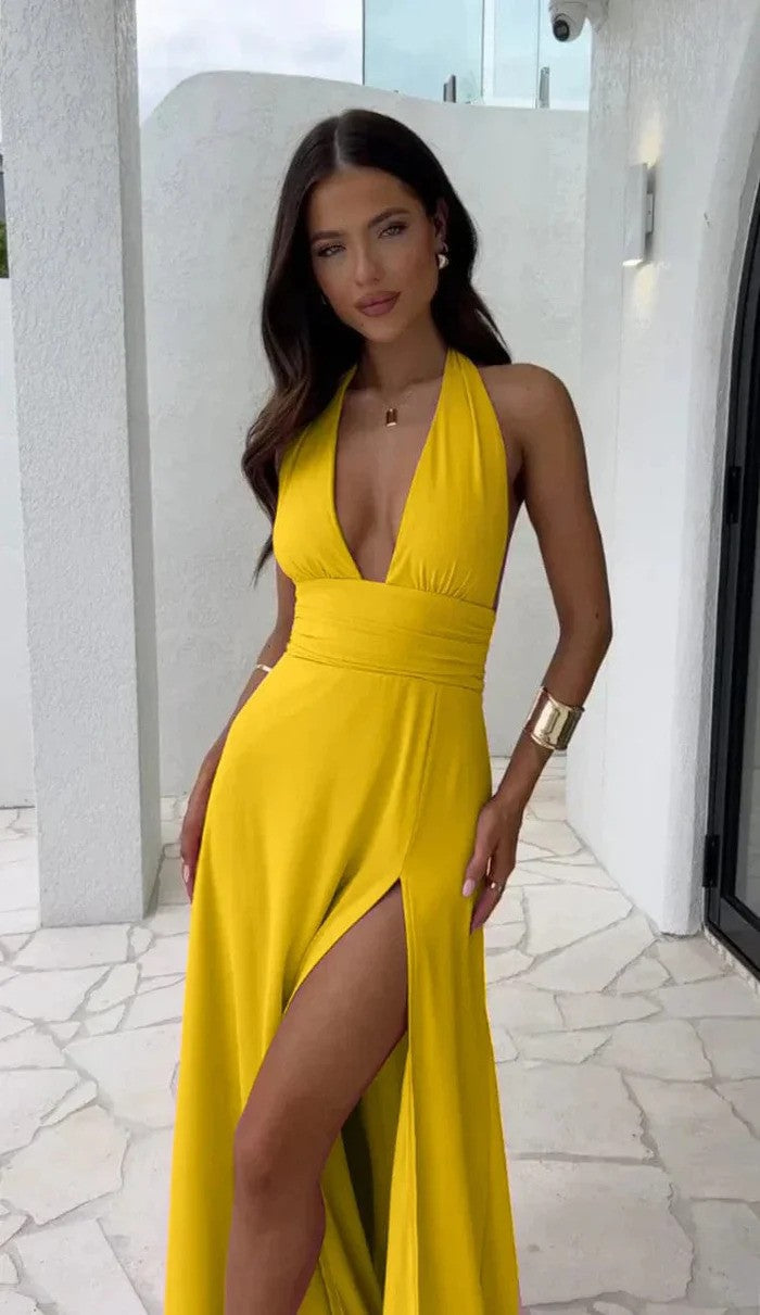 Modella in abito giallo con scollo a V e spacco alto, posa su terrazza bianca. Moda estiva elegante, abbigliamento femminile trendy.